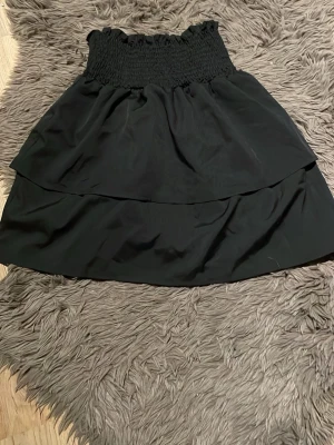 Svart volangkjol  - Svart kjol med smock i midjan och dubbla volanger. Kjolen har en kort modell. Tillverkad i ett mjukt tyg som ger ett fint fall.
