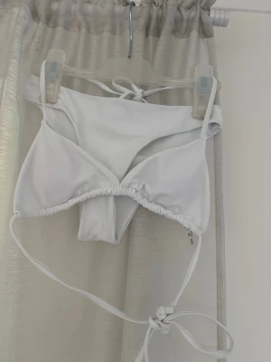 Vit trekantsbikini med knytband - Snygg vit bikini med trekantsöverdel och knytband i både rygg och nacke. Underdelen har klassisk passform och är också i helvitt. Perfekt för stranden eller poolen. Materialet känns mjukt och stretchigt. Endast använd 1 gång.