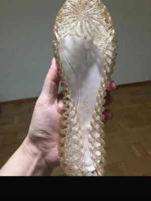 Glittriga transparenta ballerinaskor - Säljer ett par glittriga ballerinaskor i transparent plastmaterial. Skorna har ett unikt flätat mönster runt kanterna och en dekorativ blomformad detalj framtill. Perfekta för dig som vill sticka ut med en sagolik och trendig look.