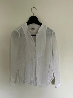 Vit blus från noa noa med knappar - Stilren vit blus från Whyred i tunn bomull med lång ärm och knappar framtill. Blusen har en klassisk krage och lätt transparent material som ger en luftig känsla. Perfekt att matcha med jeans eller kjol för en trendig look.