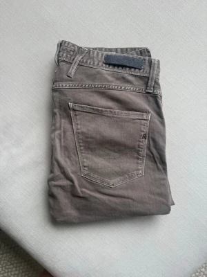 Grå Replay jeans - Säljer ett par snygga beige jeans från Replay med klassisk femficksdesign. Jeansen har diskreta sömmar och en liten logga på bakfickan. Perfekta för dig som gillar stilrena och neutrala plagg. Storlek 31/32.