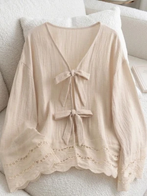 Beige blus med rosetter och spets - Supersöt beige blus med två rosetter framtill och v-ringning. Blusen har långa ärmar och fina spetsdetaljer längs ärmslut och nederkant. Tillverkad i ett tunt, luftigt tyg som känns mjukt mot huden. Perfekt för en romantisk och trendig look.