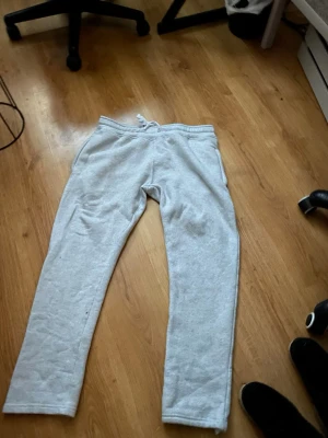 Ljusgrå mjukisbyxor från R - Ljusgrå mjukisbyxor från R i storlek M. Byxorna har en rak passform och resår med dragsko i midjan. De är tillverkade i ett mjukt och bekvämt material som passar perfekt för chill dagar. Enkla och stilrena utan tryck eller mönster. Den har tapat snöret vid ens benet där nere vid fötterna 
