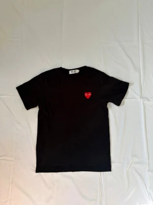 Svart Comme des Garçons Play t-shirt - Svart t-shirt från Comme des Garçons Play med det ikoniska röda hjärtat med ögon broderat på bröstet. Klassisk passform och rund halsringning. Perfekt basic med en twist för dig som gillar streetwear vibes. Är xs men passar s