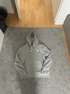 Grå hoodie med vit dragsko - En klassisk grå hoodie från ralphlauren med ficka där fram och vita snören. Hoodien är ribbad vid ärmslut och nederkant, samt en avslappnad passform. Perfekt för en chill och stilren look. Passar dig som är 165-170/xs. Tveka inte med frågor!