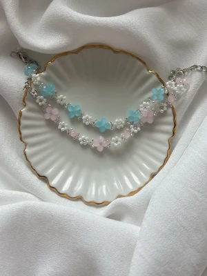 Sött armband med pärlblommor - Armband med små pärlor formade som blommor i pastellfärger. Blommorna är i ljusblått, ljusrosa och vitt, och sitter på en tunn silverfärgad kedja. Perfekt accessoar för en lekfull och trendig look. 70kr/st. Tillgänglig i andra färger.