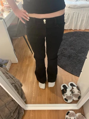 Svarta bootcut jeans med dubbla knappar - Säljer ett par svarta bootcut jeans med dubbla knappar i midjan och klassiska fem fickor. Jeansen har en snygg utsvängd passform och är perfekta för en trendig look. Materialet är stretchigt och bekvämt, vilket gör dem lätta att bära hela dagen.