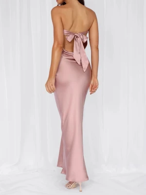 Lång rosa satinklänning med rosett - Elegant axelbandslös långklänning i denrosa satin. Klänningen har en öppen rygg med stor rosettdetalj och figurnära passform som ger en lyxig känsla. Perfekt för dig som vill sticka ut med en stilren och trendig look.