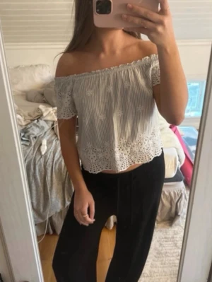  offshoulder topp från hollister  - Säljer en söt vit offshoulder topp med tunna vertikala ränder och broderade blommor. Toppen har spetskant nertill och är croppad, perfekt för sommarens alla tillfällen. Luftigt material och elastisk kant upptill för bästa passform.