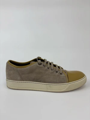 Beige Lanvin och bruna sneakers i mocka - Sneakers i beige mocka med bruna detaljer och glansig brun tå. Klassisk låg modell med snörning och vit sula. Perfekta för dig som gillar stilrena och unika färgkombinationer.