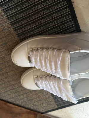 Vita höga sneakers med vita snören balenci arena  - Stilrena vita sneakers med högt skaft och klassisk design. Skorna har vita platta snören och är tillverkade i ett slätt material som ger en clean look. Perfekta för dig som gillar minimalistisk stil och vill ha ett par sneakers som funkar till det mesta. Passar 42/43