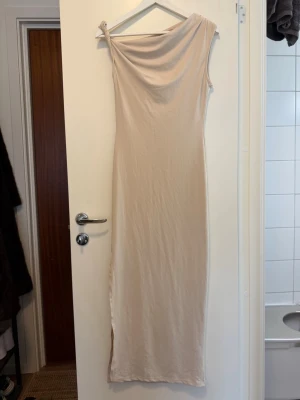 Beige långklänning - Stilren beige långklänning med smal passform. Klänningen är ärmlös och har en elegant, enkel design som ger en sofistikerad look.  Inga fler bilder.