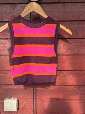 Randig ärmlös topp från Zara - Snygg ärmlös topp från Zara med breda ränder i lila, rosa och orange. Toppen är croppad och har en ribbad halsringning. Perfekt för dig som gillar färg och vill sticka ut lite extra.