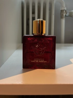 Versace Eros Flame Eau de Parfum - Versace Eros Flame Eau de Parfum i en lyxig, mörkröd glasflaska med guldigt lock. Flaskan har en fyrkantig form och pryds av Versaces ikoniska Medusa-huvud på framsidan. Perfekt för dig som gillar exklusiva och eleganta dofter. Hälften kvar