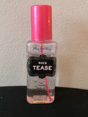 Victoria's Secret Noir Tease Body Mist - En snygg body mist från Victoria's Secret i doften Noir Tease. Flaskan är genomskinlig med svart etikett och har ett rosa lock och rosa sugrör. Perfekt att ha i väskan för en fräsch touch när som helst.