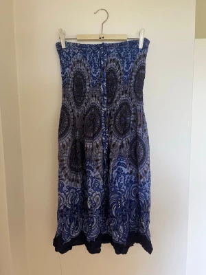 Blå klänning med mönster - Klänning i olika blå nyanser med ett detaljerat, bohemiskt mönster. Klänningen är ärmlös och har en luftig passform, perfekt för sommardagar. Tillverkad i ett lätt material som ger en skön känsla. Köpt på kreta.