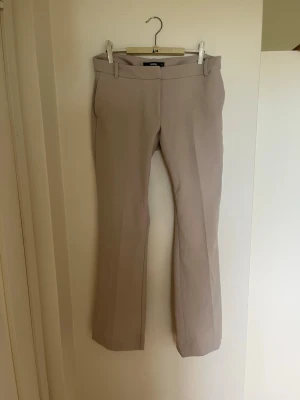Beige kostymbyxa med pressveck - Snygga beige kostymbyxor med utsvängda ben. Byxorna är mid-waist. Perfekta för en stilren och trendig look.