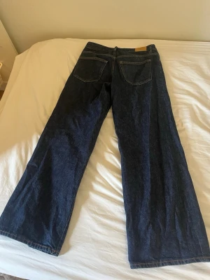 Mörkblå raka jeans med låg midja - Säljer ett par mörkblå jeans med rak passform och lågvmidja. Jeansen har klassiska fem fickor och är tillverkade i kraftigt denimtyg. Perfekta för dig som gillar en tidlös och avslappnad stil.