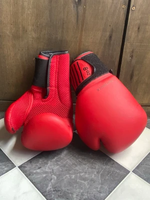 Röda boxningshandskar 8 oz Outshock - Säljer ett par röda boxningshandskar från Outshock i storlek 8 oz. Handskarna har kardborreknäppning och är tillverkade i syntetmaterial med meshdetaljer för ventilation. Perfekta för träning eller sparring inom boxning.