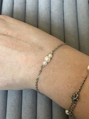 Tunt silverarmband med pärlor - Ett stilrent armband med tunn silverfärgad kedja och tre vita pärlor i mitten. Perfekt för dig som gillar minimalistiska smycken med en elegant touch. Justerbar längd med karbinlås.