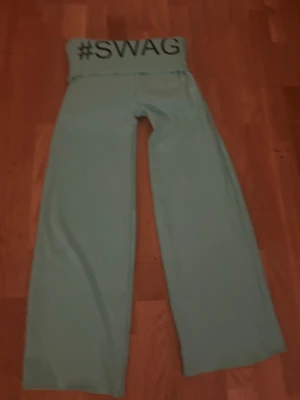 Ljusgröna mjukisbyxor med #SWAG-tryck - Ljusgröna mjukisbyxor med bred resår i midjan och svart #SWAG-tryck framtill. Byxorna har raka, vida ben och är gjorda i ett mjukt och bekvämt material. Perfekta för en avslappnad och trendig stil.Om du intreserad jag vill bara förvarana att dom här byxorna är från en liten företag som hetter jennifer.☺️