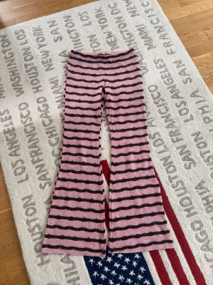 Rosa och bruna randiga leggings - Säljer ett par unika leggings med rosa och bruna vågiga ränder. De har utsvängda ben och är gjorda i ett mjukt, stretchigt material som känns skönt mot huden. Perfekta för dig som vill sticka ut med ett coolt mönster och bekväm passform.