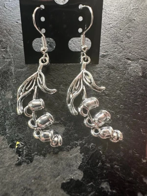 Silvriga örhängen med blomdetaljer - Säljer ett par snygga silvriga örhängen i form av hängande blommor med blad. De har en glansig finish och är tillverkade i metall. Perfekta för dig som gillar unika och naturinspirerade accessoarer.