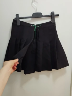 Kpop kortkjol med öppning och rosett - Kpop stil, svart plisserad kortkjol som är helt öppen med snörning så benen syns; supersnyggt över ett par biker shorts eller tights. För mått se bilderna, men eftersom den är öppen så går det justera storleken beroende upp hur man knyter den. Går att förlänga på ett coolt sätt med en kedja t ex.. Kolla gärna mina andra annonser <3