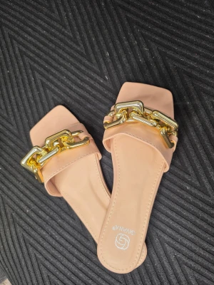 Beiga sandaler med guldkedja - Stilrena beiga sandaler från GINA TRICOT med fyrkantig tå och bred rem dekorerad med en chunky guldfärgad kedja. Tillverkade i konstläder för en trendig look. Perfekta för dig som vill ha något extra till outfiten.