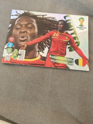 FIFA World Cup spelkort Belgien - Säljer ett färgglatt spelkort från FIFA World Cup Brasil med Romelu Lukaku från Belgien. Kortet har en glansig yta, tydliga stats och landslagsflagga. Perfekt för samlare eller dig som gillar fotbollsspel och trading cards.
