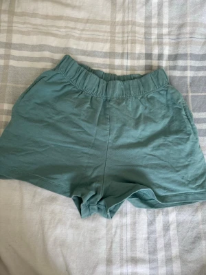 Gröna shorts från SOC i bomull - Säljer ett par ljusgröna shorts från SOC i mjuk bomull. De har elastisk midja och en avslappnad passform, perfekta för varma dagar eller träning. Klassisk enkel design utan mönster eller extra detaljer.