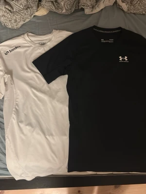 Bundle med 2 Compressionshirts - Den vita är från Sondico i Storleken M. Den svarta är från Under Armour i Storleken M. Perfekt för den som gymmar eller planerar på att börja. 
