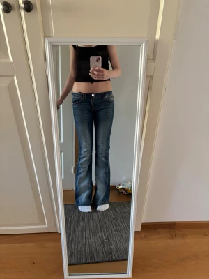 Blå bootcut jeans från Gina Tricot  - Säljer ett par blå bootcut jeans från Gina Tricot i storlek 170. Jeansen har låg midja, fickor med snyggt mönster på dem. Perfekta för dig som gillar en retro vibe och vill ha ett par utsvängda jeans. Har upprivning där bak men det kan sys ihop snabbt, det är inte heller så synligt även om man inte syr ihop.