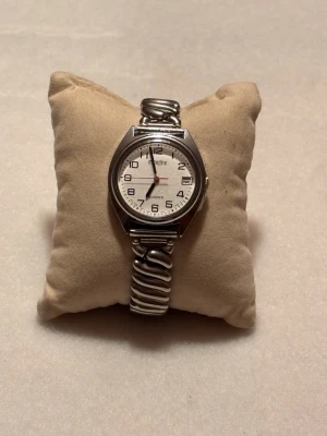 Moretime Klassisk silverfärgad klocka Quartz - Stilren klocka från Quartz med vit urtavla och tydliga svarta siffror. Boetten är rund och armbandet är i silverfärgad metall med vågig design. Klockan har datumvisning och klassisk look som passar till det mesta.