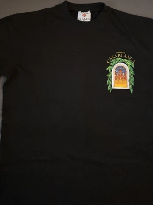 Svart Casablanca t-shirt med tryck - Snygg svart t-shirt från Casablanca med färgglatt tryck på bröstet som föreställer en port med texten 'Avenida Casablanca'. Klassisk passform och rund hals. Perfekt för dig som vill ha en stilren tee med unik detalj.