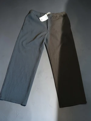 Tvåfärgade mjukisbyxor med dragsko - Unika mjukisbyxor med ena benet i svart och andra i grått. Vida ben och elastisk midja med vit dragsko. Tillverkade i mjukt, ribbat material som ger en avslappnad och trendig look. Perfekta för dig som vill sticka ut med din stil.