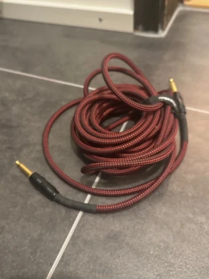 Supreme GCW  instrumentkabel  - Säljer en röd och svart flätad instrumentkabel med 6,3mm (1/4 tum) guldpläterade jackkontakter i båda ändar. Kabeln är flexibel och har ett slitstarkt tygöverdrag, perfekt för gitarr, bas eller andra instrument.