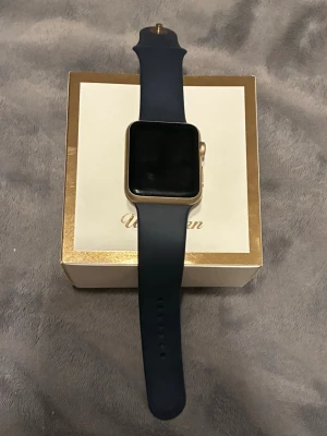 Apple Watch Series 2 42mm guld - Snygg Apple Watch Series 2 med 42mm boett i guld och svart sportarmband i silikon. Klockan har en fyrkantig skärm och pulsmätare på baksidan. Batteriet är urladdat. Mycket bra skick som ny. Orginalpris: 2500kr 