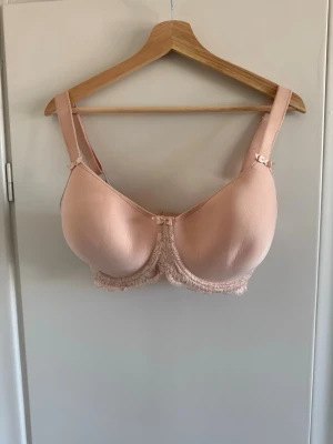 Ljusrosa vadderad bh med spets - Söt ljusrosa bh med vadderade kupor och dekorativa små rosetter vid axelbanden. Bh:n har spetsdetaljer längs nederkanten och breda, justerbara axelband för extra komfort. Materialet är mjukt och slätt, perfekt under tighta toppar.