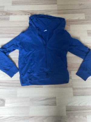 Blå zip hoodie med huva - En enkel blå hoodie med dragkedja framtill och huva. Hoodien har långa ärmar och ribbade muddar vid ärmslut och nederkant. 