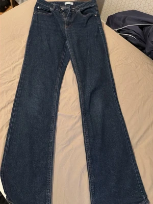 Mörkblå bootcut jeans - Säljer ett par mörkblå bootcut jeans med klassisk femficksdesign och hög midja. Jeansen har vida ben och är tillverkade i ett mjukt denimtyg som ger en snygg siluett. Perfekta för dig som gillar retrovibbar och vill ha ett par jeans som sticker ut.