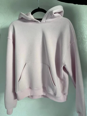 Ljusrosa hoodie med huva - En stilren ljusrosa hoodie med huva och magficka. Tröjan har ribbade muddar vid ärmslut och nederkant samt en avslappnad passform. Perfekt för dig som gillar en enkel men snygg look. Materialet känns mjukt och bekvämt. Hoodien är bara använd ett fåtal gånger, en liten sminkfläck vid halsen men borde gå bort i tvätten innan jag skickar paketet. Annars inga synliga skador❤️ (Nypris 360kr)