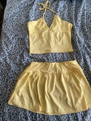 Gult set med topp och kjol - Säljer ett gulligt gult set med en halterneck topp med v-ringning och en matchande kort kjol. Setet är gjort i ett mjukt, stretchigt material som känns bekvämt mot huden. Perfekt för dig som vill ha en söt och somrig look.