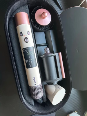 Dyson Airwrap hårstyler i etui - Säljer en Dyson Airwrap hårstyler i beige och roséguld med flera tillbehör. Kommer i ett elegant svart etui. Perfekt för att styla håret med olika borst- och locktillbehör. Enkel att använda med tydliga knappar och instruktioner på handtaget.