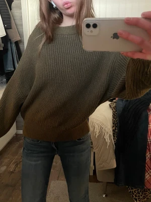 Olivgrön oversized stickad tröja - Säljer en olivgrön oversized stickad tröja med grovstickad struktur och breda ärmar. Tröjan har rund halsringning och ribbade muddar vid ärmslut och nederkant. Perfekt för lager på lager och en avslappnad look.