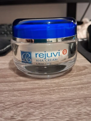 Rejuvi AHA Cream 50g glasburk - Rejuvi AHA Cream i en elegant glasburk med blått lock. Krämen kommer i en rund transparent burk med silverdetaljer och innehåller 50g. Perfekt för dig som vill ha en exfolierande ansiktskräm med AHA-syra. Endast testad.