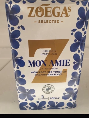 Zoégas Mon Amie jubileumskaffe - Zoégas Mon Amie jubileumsutgåva 2026, mörkrost med toner av rabarber och viol. Förpackningen är vit med blå blommor och guldiga detaljer, framtagen i samarbete med Rörstrand.