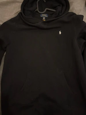 Svart hoodie från Polo Ralph Lauren - Svart hoodie från Polo Ralph Lauren med klassisk huva och känguruficka. Liten vit broderad logga på bröstet. Mjuk insida och stilren design, perfekt för en avslappnad look. Tvär fett tröja det är 18/20 som motsvarar S. Skicka gärna bud.