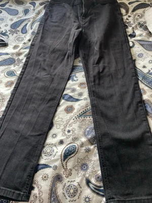 Svarta raka jeans - Säljer ett par svarta jeans med rak passform och klassisk femficksdesign. Jeansen har bälteshällor och dragkedjegylf. Materialet är denim i bomull. Perfekta för dig som gillar en enkel och stilren look.