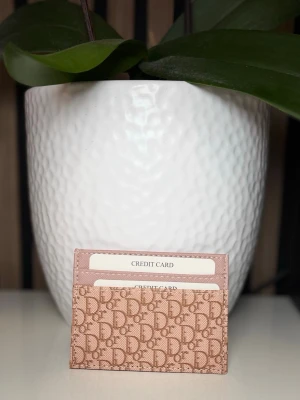 Beige  korthållare med monogram -  Slimmad design med flera kortfack, perfekt för dig som vill ha stilren och lyxig accessoar i väskan. Tillverkad i canvas med läderdetaljer.